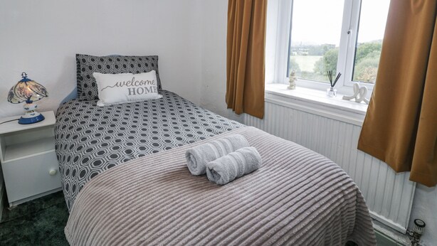 A neatly arranged bedroom with a bed, a bedside table, a window with curtains, and a view of the outdoors. - Old Post Office (Blaenau Ffestiniog)