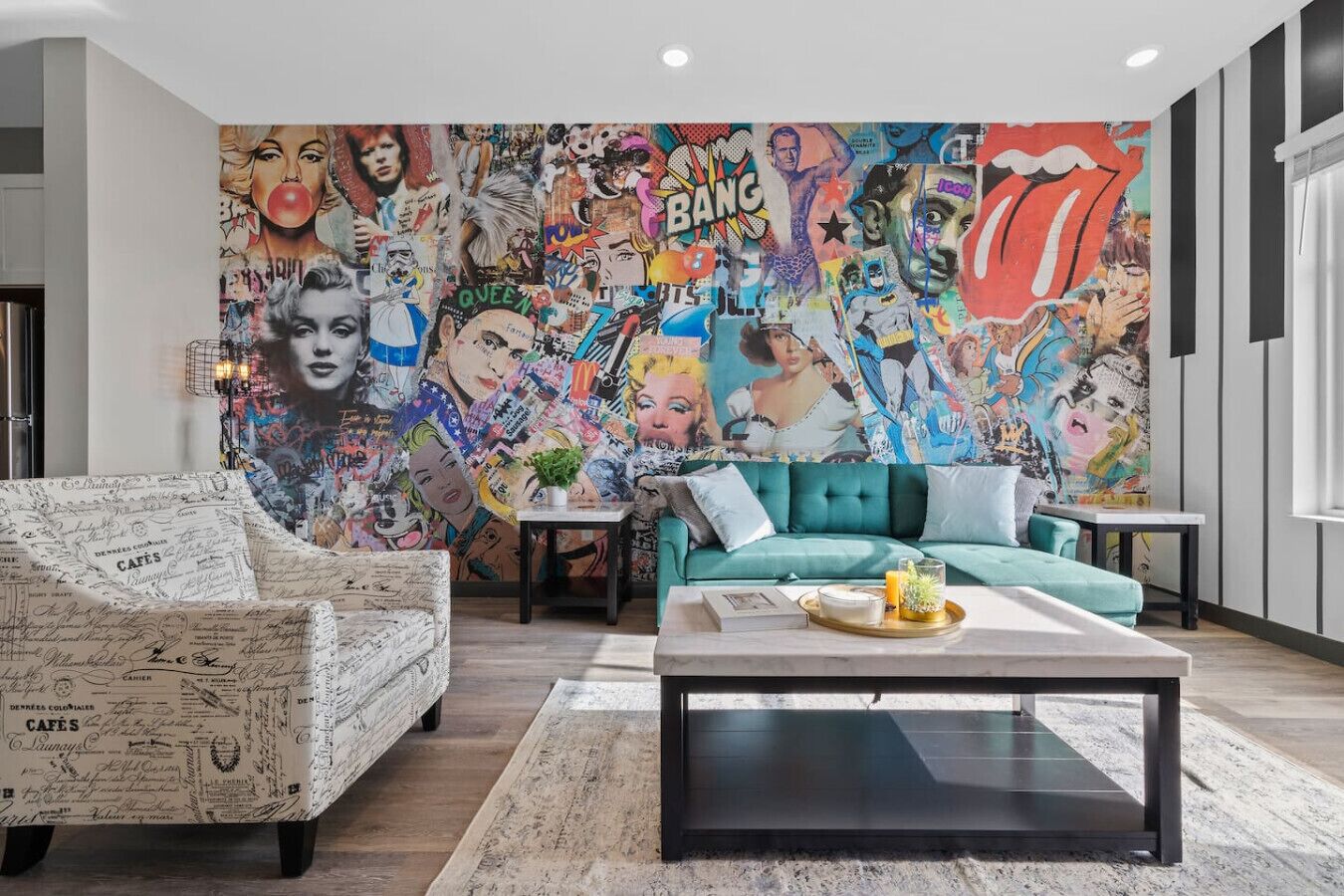 A living room with a vibrant mural, a teal sofa, a white armchair, and a coffee table with a tray.