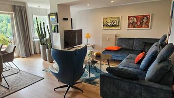 Ein modernes Wohnzimmer mit grauem Sofa, blauem Sessel, Fernseher und Kunstwerken an der Wand.