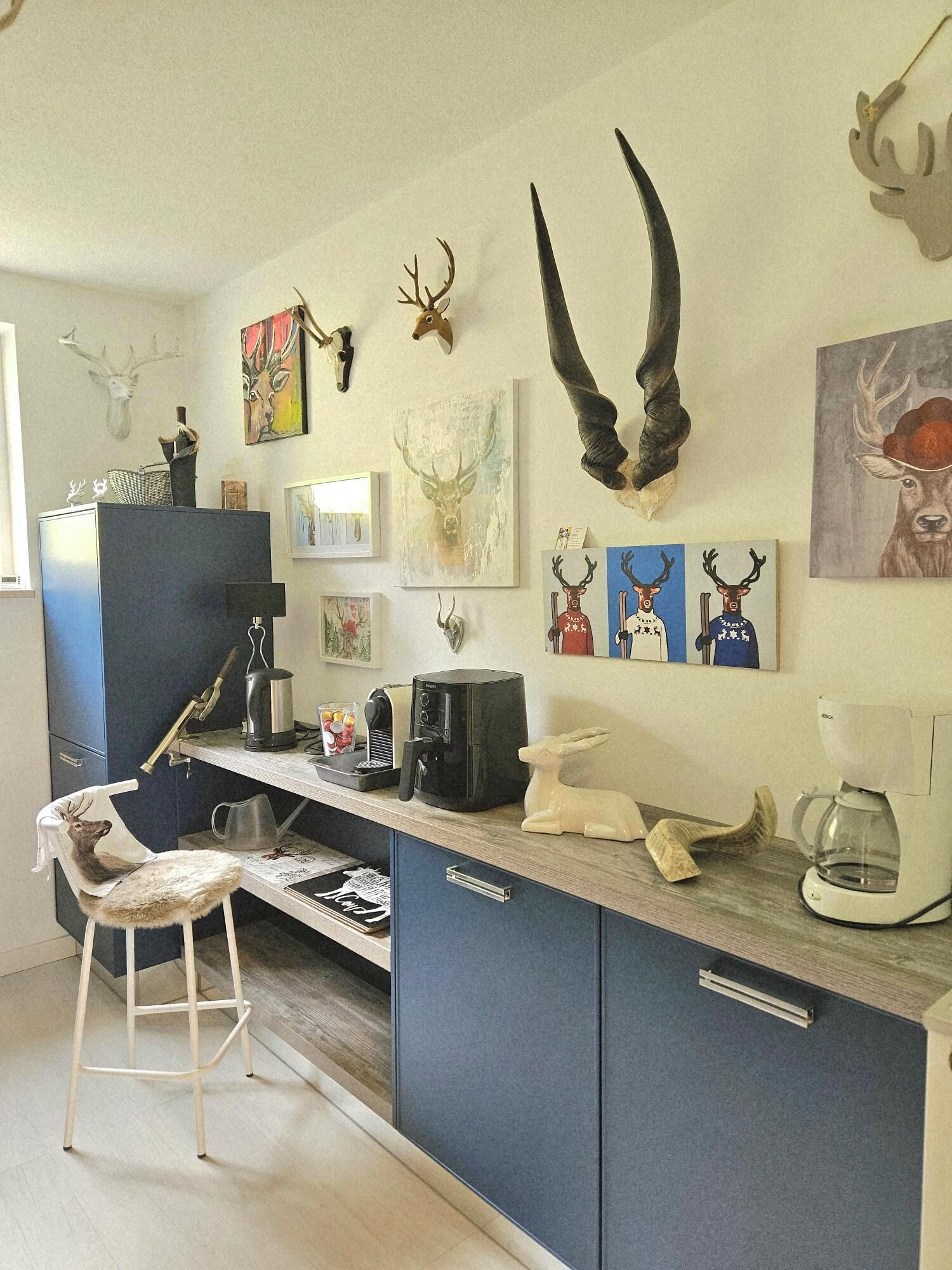 Una cucina moderna con angolo bar, dotata di macchina per caffè, bollitore e lavello. Si notano corna di cervo appese e opere d'arte sulla parete.