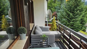 Ein Balkon mit einer Couch, einem Tisch und Stühlen, umgeben von Topfpflanzen und einem Geländer.