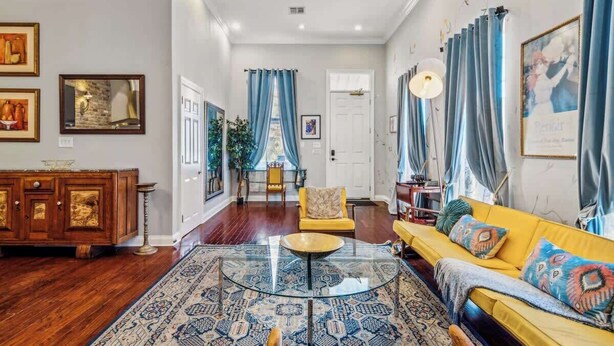A spacious living room with a wooden floor, a yellow sofa, a glass coffee table, and a patterned rug. - Sunny 5BR Villa w/ Heated Pool & Courtyard Oasis (New Orleans)