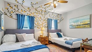 A hotel room with two beds, a ceiling fan, a cityscape painting, and a patterned carpet. - Sunny 5BR Villa w/ Heated Pool & Courtyard Oasis (New Orleans)