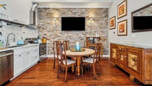 A kitchen with a brick wall, wooden cabinets, a round dining table, and a built-in oven. - Sunny 5BR Villa w/ Heated Pool & Courtyard Oasis (New Orleans)