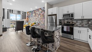 A modern kitchen with white cabinets, stainless steel appliances, and a colorful collage wall.