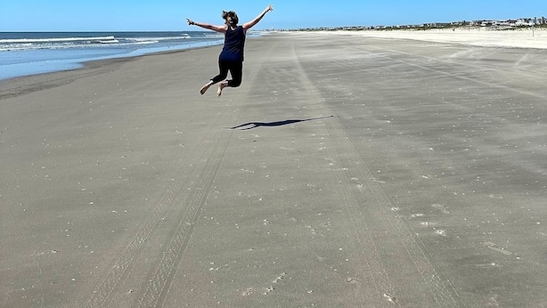 Une personne sautant sur une vaste plage déserte, sous un ciel bleu et dégagé.