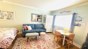 A bedroom with a bed, a blue sofa, a small table with a lamp, a chair, a rug, and a wardrobe.