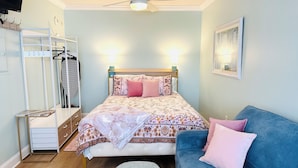 Une chambre à coucher avec un lit, un canapé bleu, une armoire et un ventilateur de plafond.