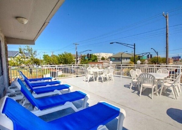 A covered outdoor seating area with blue lounge chairs and white tables and chairs.