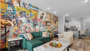 A modern living room with a vibrant mural, a green sofa, a coffee table, and a kitchen area in the background. - Quiet 1BR Apt - 8min to Broadway, Free Wifi! (Nashville)