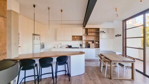 A modern kitchen with a central island, bar stools, a dining table with chairs, and a large window providing a view of the outdoors. - Shlomo Hamelekh Topaze (Tel Aviv)