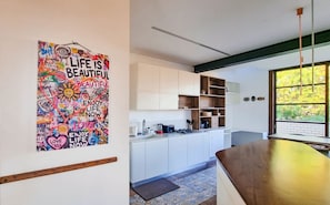 A modern kitchen with white cabinets, a wooden countertop, and a large window with a view of greenery.