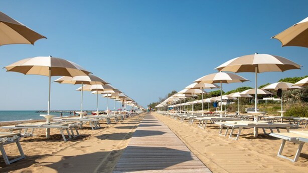 A beach with rows of sun umbrellas and lounge chairs along a wooden walkway. - Vacation village Jesolo Lodge Comfort for 5 persons (Lido di Jesolo)