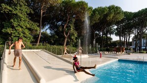 A swimming pool with a water slide, trees, and a small building in the background. - Vacation village Jesolo Lodge Comfort for 5 persons (Lido di Jesolo)