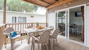 A covered outdoor patio with a table and chairs, a wicker chair with a bag, and a view of a mobile home in the background. - Vacation village Jesolo Lodge Comfort for 5 persons (Lido di Jesolo)