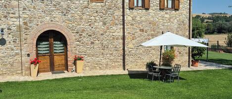 A stone building with a tiled roof, a brick archway entrance, and a small patio with a table and chairs.