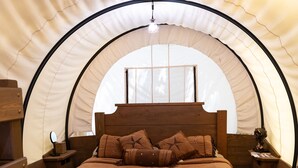 A cozy tent-style bedroom with a wooden bed, a nightstand, and a small table with a lamp.
