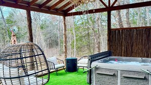 A covered outdoor patio with a hot tub, seating area, and artificial grass.