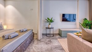 A modern hotel room with a bed, a small seating area, a TV, and a plant. - Official Mercury Suites | With Rooftop Pool Access (St. Julian`s)