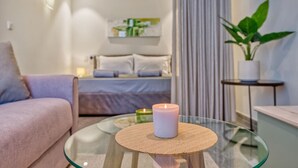 A modern living room with a glass coffee table, a sofa, a bed with a view, and a potted plant. - Official Mercury Suites | With Rooftop Pool Access (St. Julian`s)