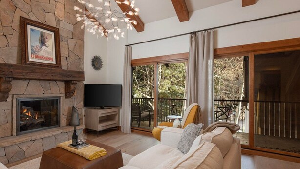 A living room with a stone fireplace, a flat-screen TV, a sofa, and a balcony with outdoor furniture. - Villa Valhalla | 9 - 2 Bedroom Loft Diamond (Vail)