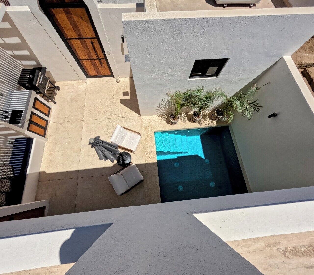 Una piscina en la azotea con cubierta azul, una puerta de madera y un pequeño jardín con plantas en macetas.