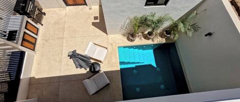 Una piscina en la azotea con cubierta azul, una puerta de madera y un pequeño jardín con plantas en macetas.