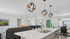 A modern kitchen with a central island, a dining area, and a living space with a sofa. - Scottsdale Sunstone Villa, Modern 6BR w/ Private Pool & Spa, Walk to Old Town (Scottsdale)