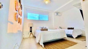 Un dormitorio con dos camas, un ventilador de techo, una ventana y una obra de arte en la pared.