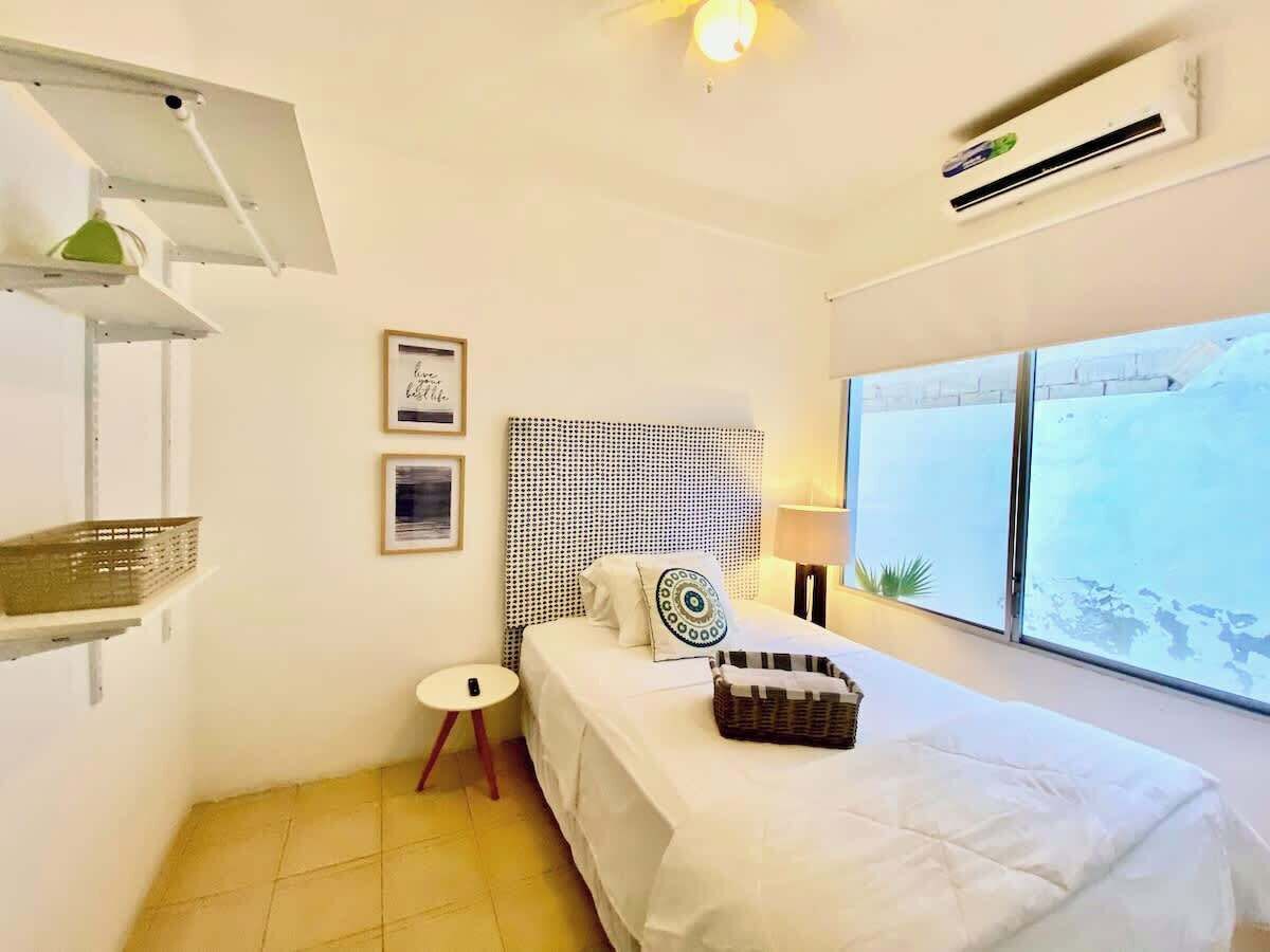 Ein Schlafzimmer mit Bett, Nachttisch, Lampe, einer Wandregal und einem Fenster mit Blick.