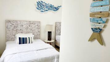 Ein Schlafzimmer mit einem gemusterten Kopfteil, einem Bett mit weißer Bettwäsche, einem Nachttisch mit Lampe und einer Wanddekoration mit Strand-Schildern.