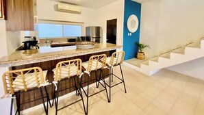 Una cocina moderna con una isla central, taburetes de bar y una escalera.
