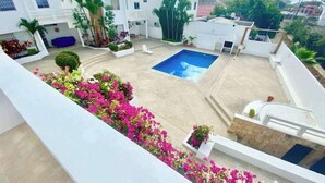 Una terraza con piscina, edificios blancos y vegetación circundante.