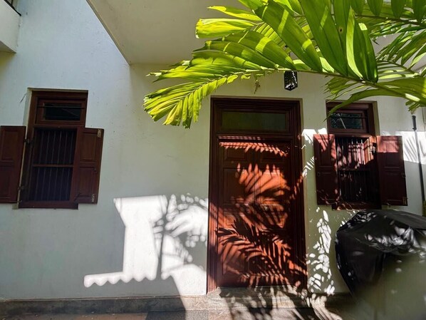 A building with a central door, two windows with shutters, and a large plant in the foreground. - 1-bedroom cozy apartment in the heart of Colombo (Colombo)