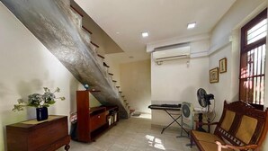 Ein geräumiger Wohnbereich mit Treppe, einem Klavier, einem Ventilator und einem Holzstuhl.
