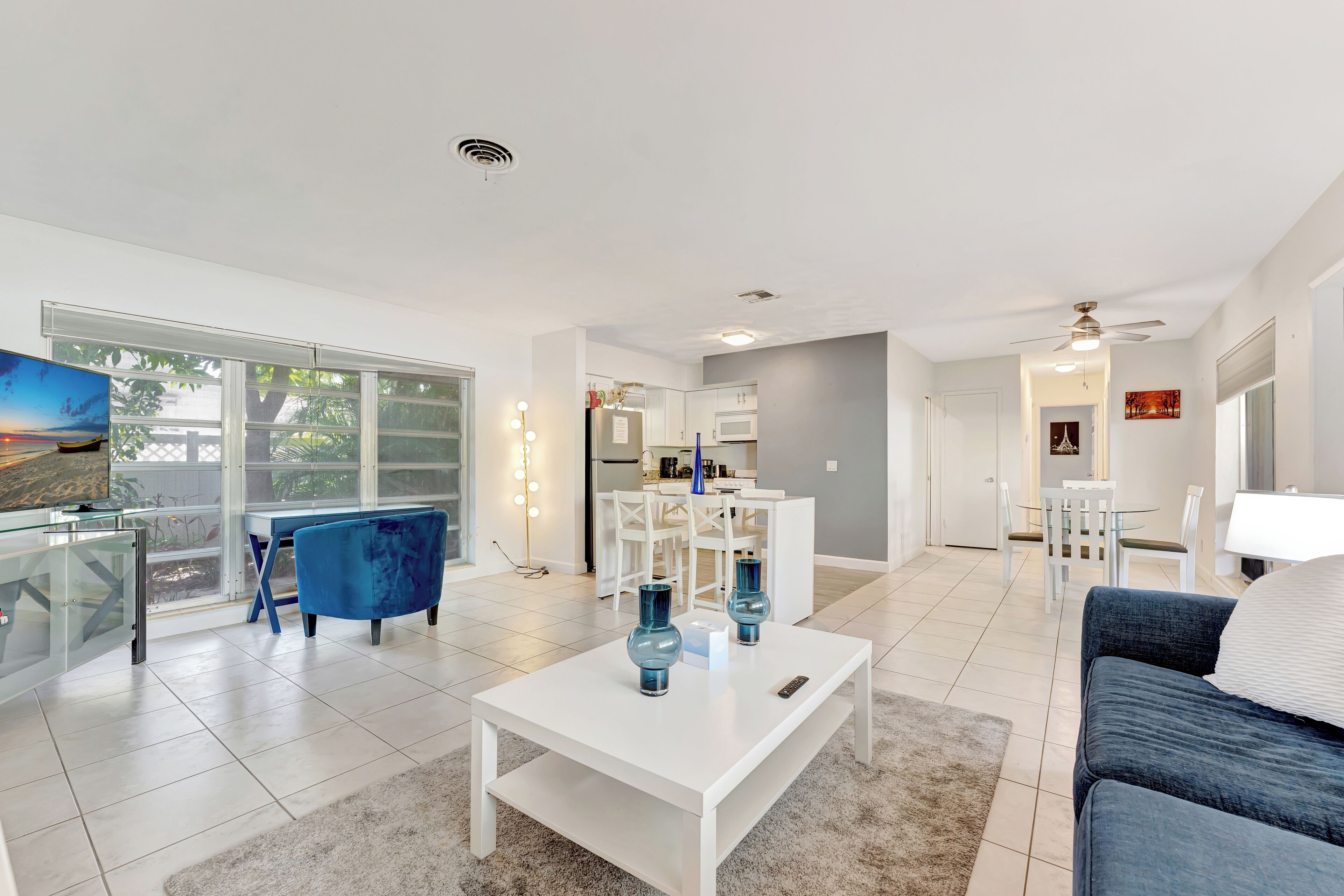 A spacious living room with a white coffee table, blue chairs, and a TV.