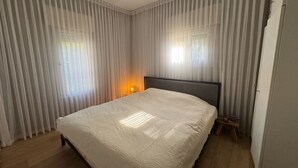 Un dormitori amb llit, sòl de fusta i cortines de tela fina.