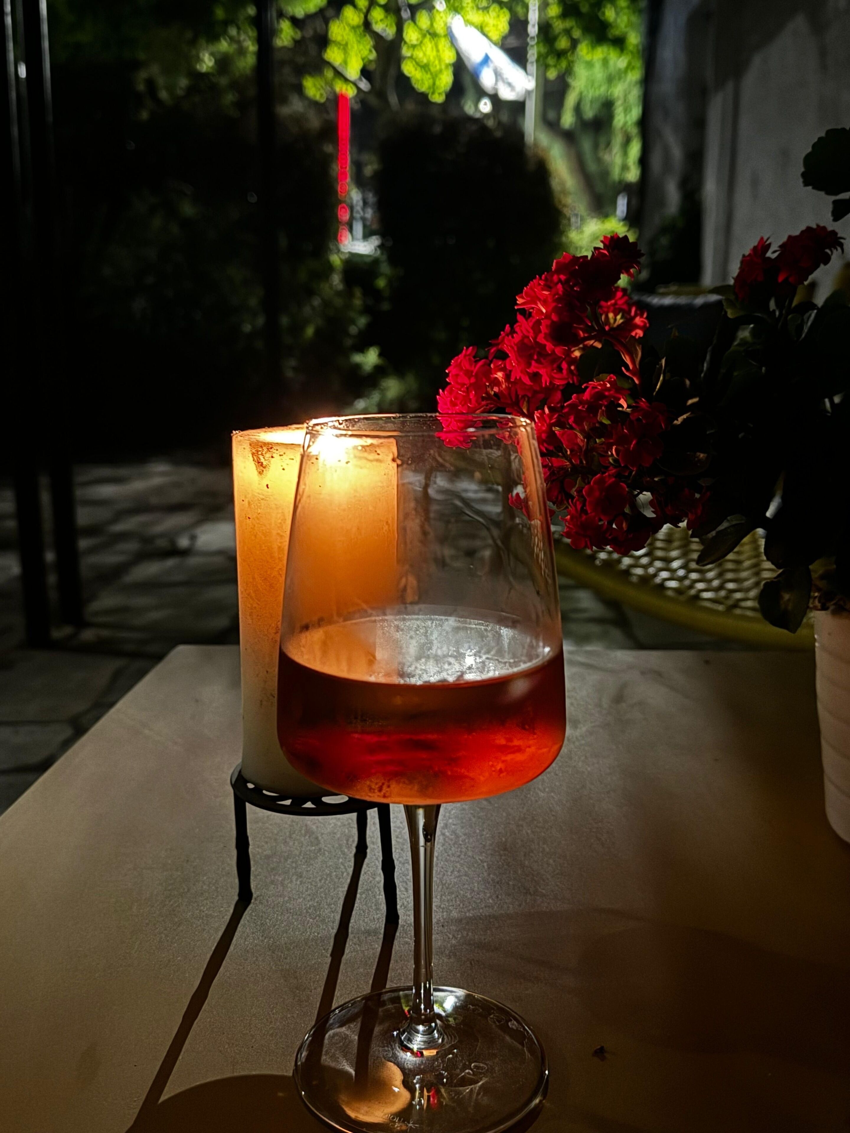 Una vela y un vaso de líquido rojo sobre una mesa al aire libre.