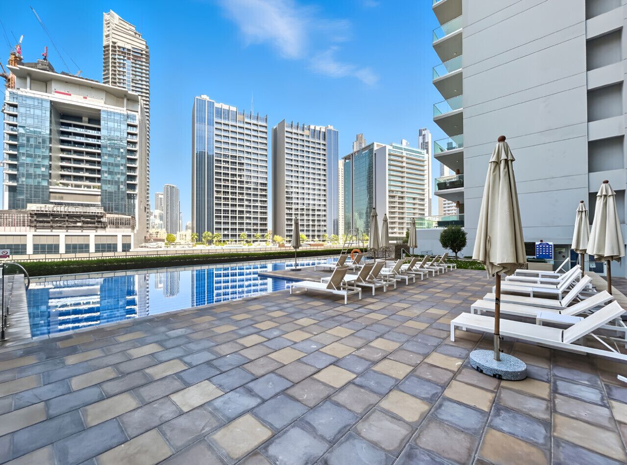 A rooftop pool area with lounge chairs and umbrellas, surrounded by high-rise buildings.