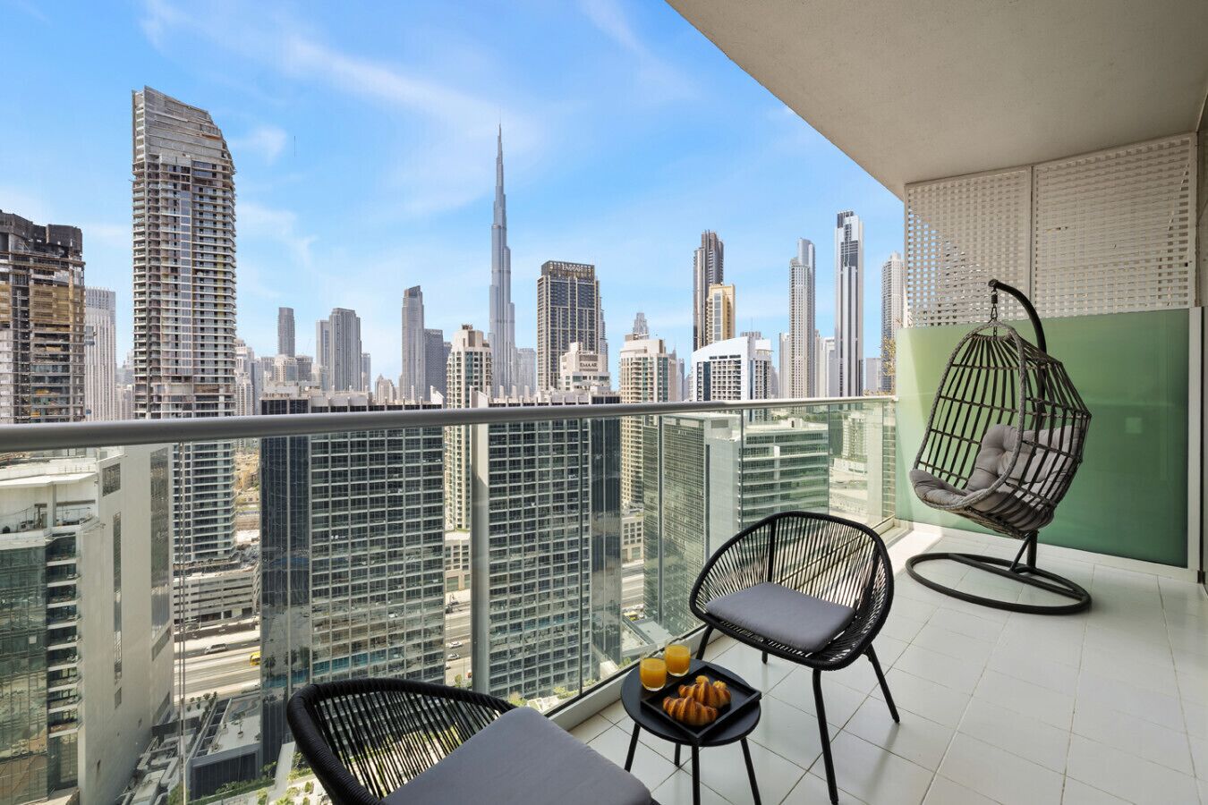 Un balcón con dos sillas, una mesa con croissants y jugo, y vista al horizonte de la ciudad.