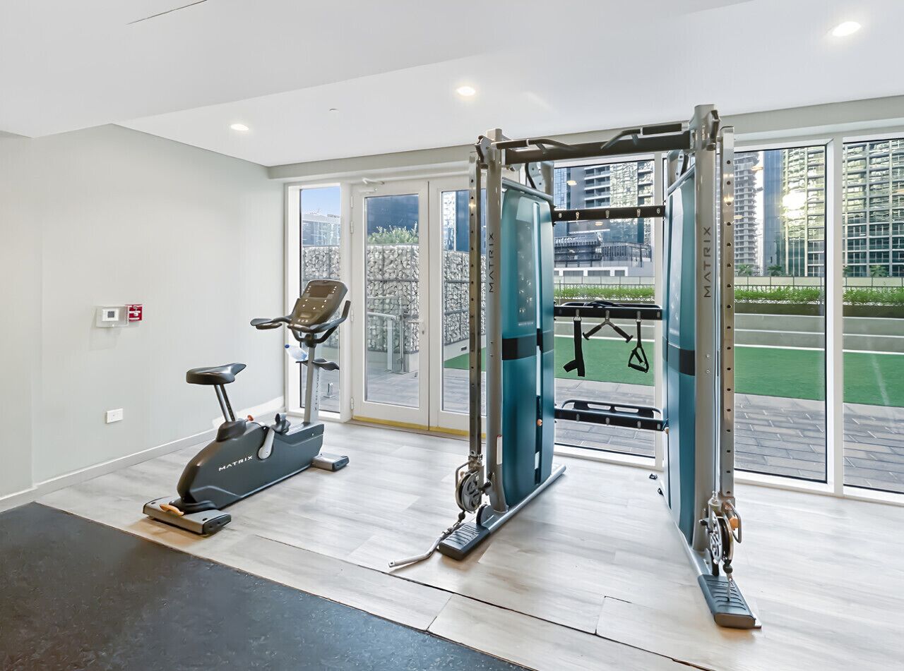 Une salle de sport équipée de machines de cardio, de postes d’entraînement en musculation et de grandes fenêtres donnant sur l’extérieur.