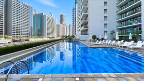 A swimming pool with lounge chairs and umbrellas, surrounded by high-rise buildings.