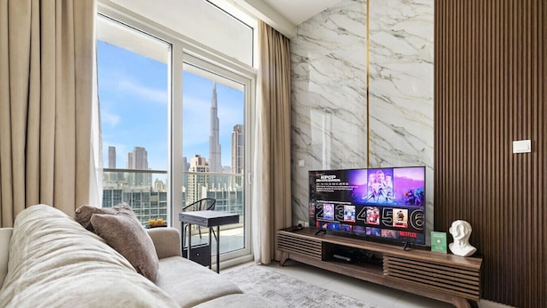 A modern living room with a large flat-screen TV, a sofa, and a dining area with a table and chairs.