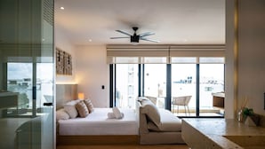 Ein modernes Schlafzimmer mit Bett, Sofa, Deckenventilator und großen Fenstern mit Blick auf die Stadt.