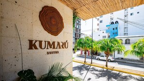 Ein Hotel Eingang mit einem großen Schild mit der Aufschrift "KUMARÚ SUITES" und einem auffälligen Holzelement darüber.