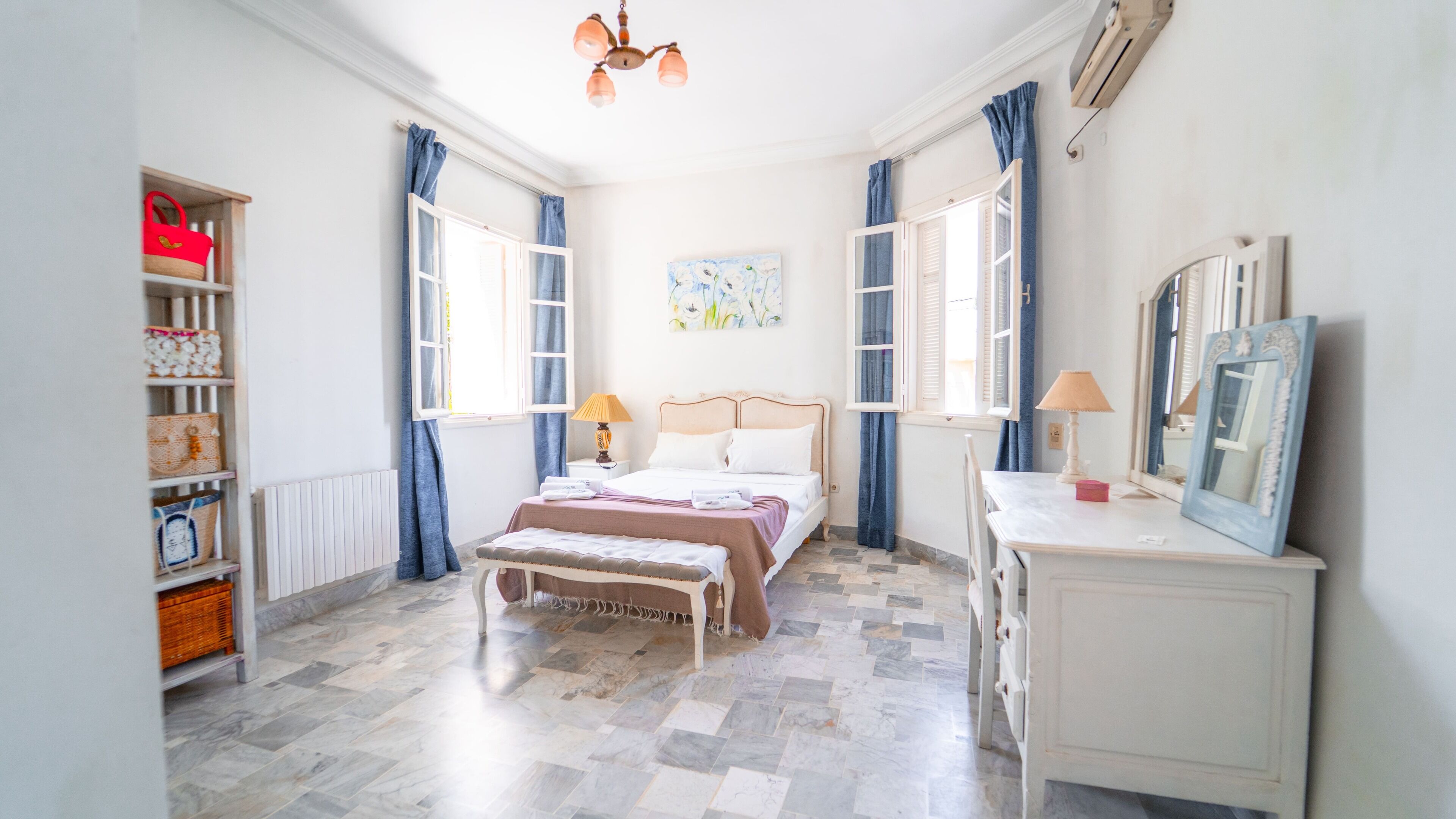 A bedroom with a bed, bedside table, lamp, dresser, and a shelf with baskets.