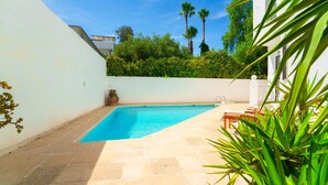 A rectangular swimming pool with a tiled deck, surrounded by a white wall and lush greenery. - Authentique Villa Tunisoise Avec Piscine Marsa (La Marsa)