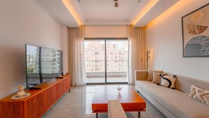 A modern hotel room with a large flat-screen TV, a sofa, a coffee table, and a view of the cityscape through the balcony doors. - Rd Parcs Appartement Neuf aux Jardins De Carthage (Tunis)