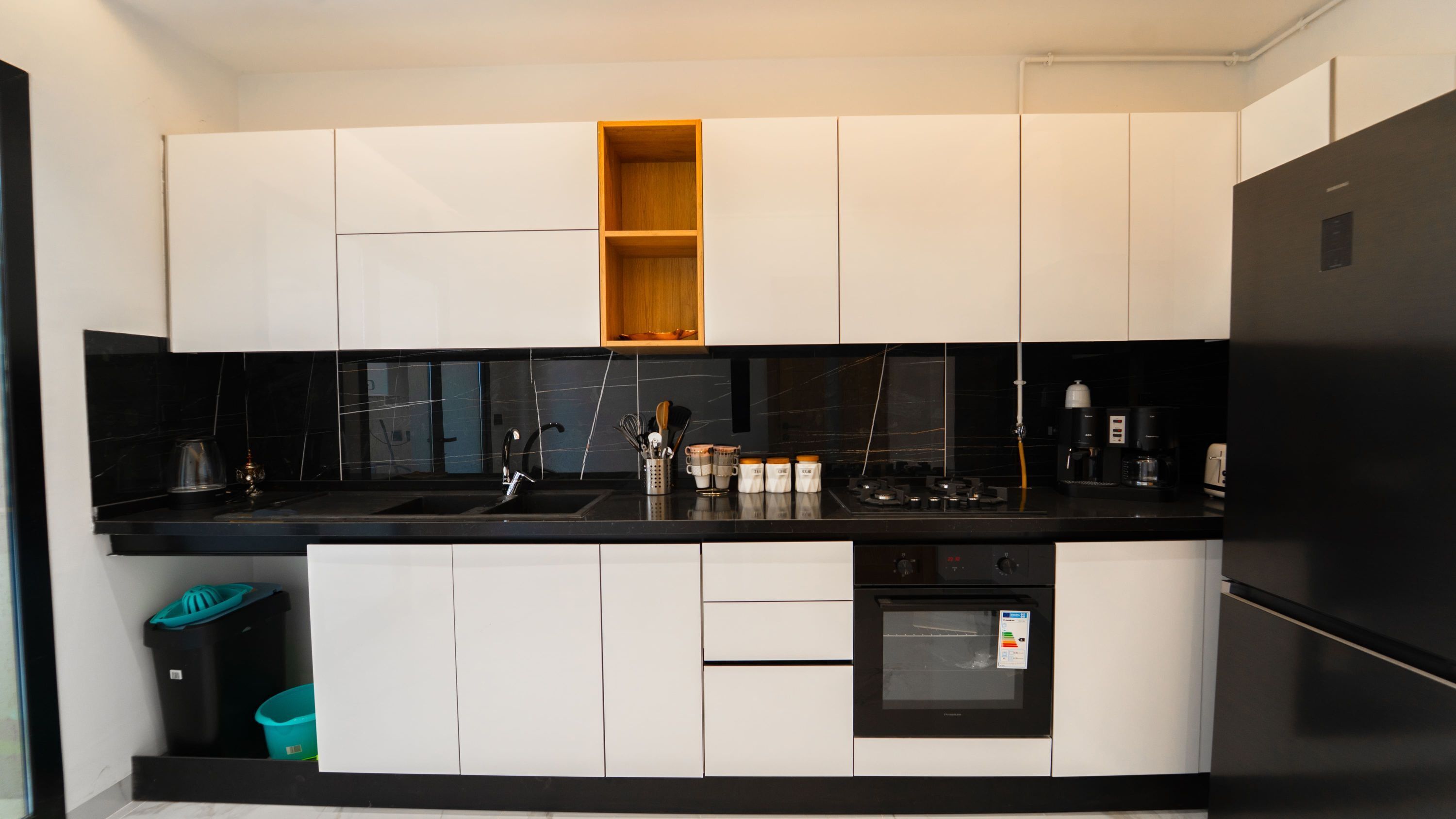 A modern kitchen with white cabinetry, a black countertop, and a built-in oven.