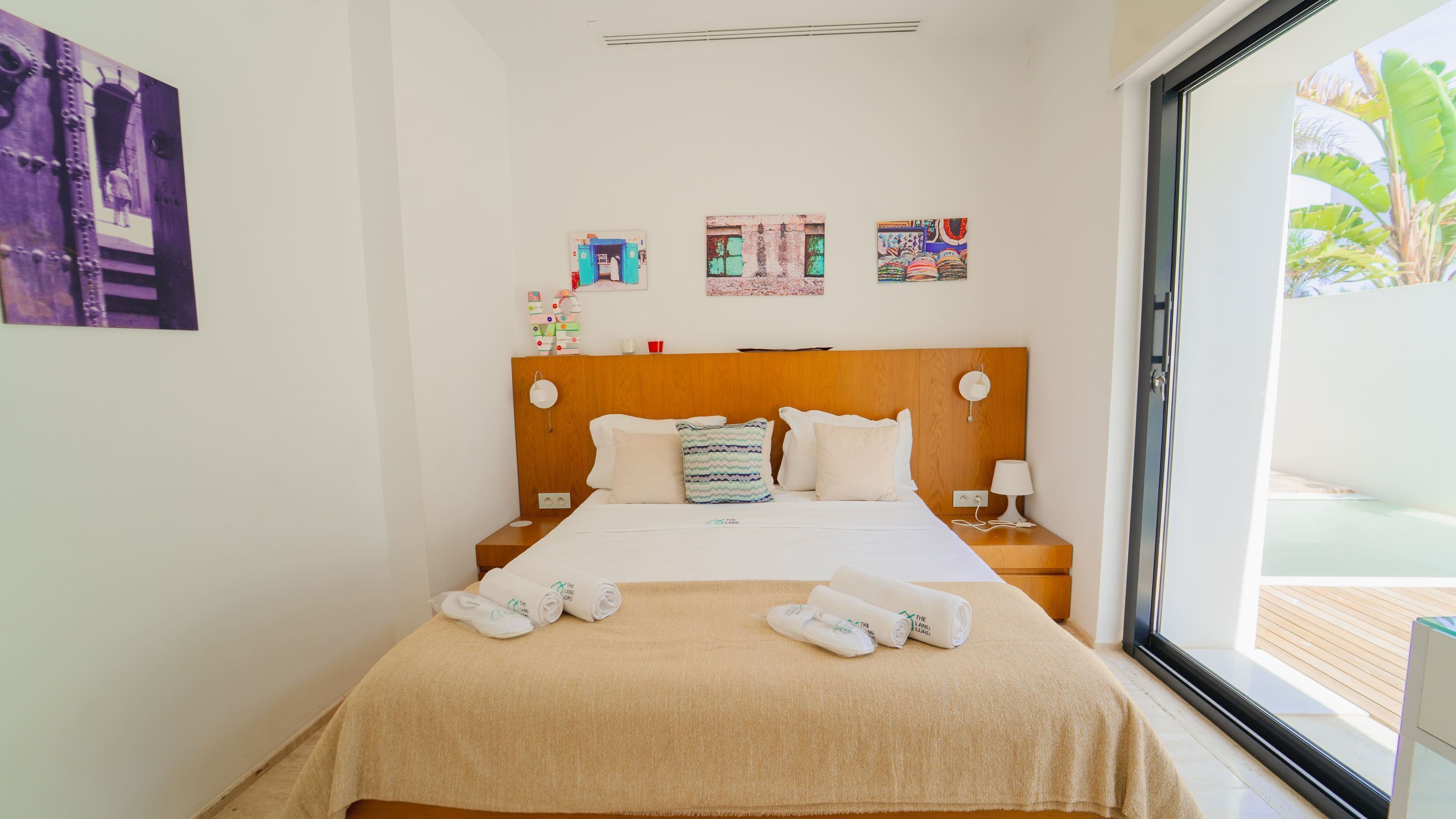 A hotel room with a bed, two bedside tables, a window with a view, and wall art.